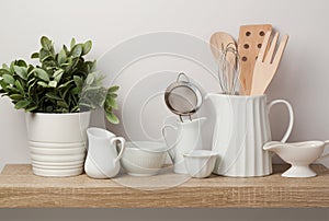 Kitchen utensils and dishware on wooden shelf.