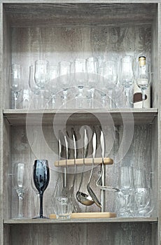 Kitchen utensils, glasses on the shelves in a wooden cabinet