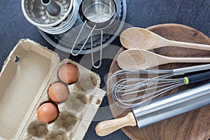 Kitchen utensils and ingredient concept, measuring cups with whisk, wooden spoon and fresh eggs.