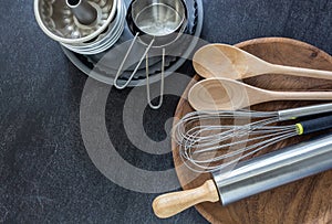 Kitchen utensils, measuring cups, whisk and wooden spoon on dark background
