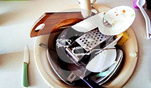 The kitchen utensils in the wash basin need to be washed. A pile of dirty dishes in the kitchen sink.