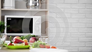Kitchen view with microwave oven and fresh vegetables and fruit on the table