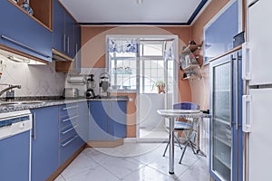 Kitchen with a wall full of plain blue cabinets with cherry wood details, gray granite countertops and stoneware floors