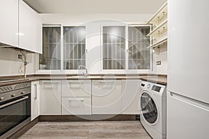 kitchen with white cabinets, brownstone worktops, twin barred windows and a white washing machine and fridge photo