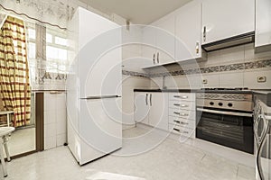 Kitchen with white furniture, a large solitary refrigerator and access