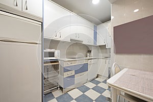 Kitchen with white wood cabinets with blue accents with matching color tiles with white stone countertops and white built-in