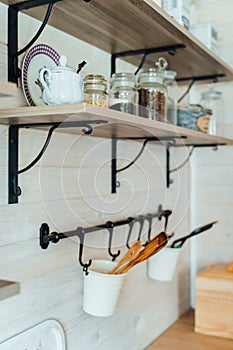 Kitchen wooden shelf with glass jars with coffee and tea leaves and accessories, blue sugar bowl with spoon. Buckets with wooden