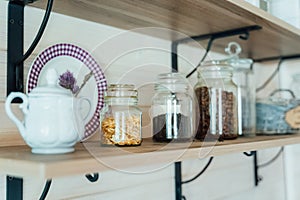 Kitchen wooden shelf with glass jars with coffee and tea leaves and accessories, blue sugar bowl with spoon. Cozy interior in a