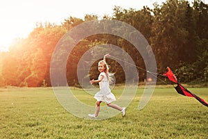 Kite is behind child. Happy girl in white clothes have fun in the field. Beautiful nature