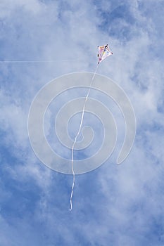 Kite flying high up in blue sky with long white streamer trailling below it