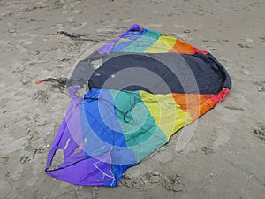 Kite in rainbowcolors with black threads laying on the beach of Velsen Netherlands