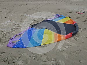 Kite in rainbowcolors with white threads laying on the beach of Velsen Netherlands