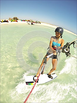 Kite surfing girl in sexy swimsuit with kite in sky on board in blue sea riding waves with water splash. Recreational activity,