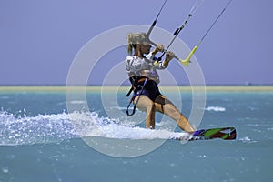 Kite surfing girl in sexy swimsuit with kite in sky on board in blue sea riding waves with water splash. Recreational activity