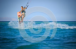 Kite surfing girl in sexy swimsuit with kite in sky on board in blue sea riding waves with water splash. Recreational activity