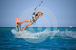 Kite surfing girl in sexy swimsuit with kite in sky on board in blue sea riding waves with water splash. Recreational activity