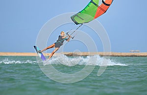 Kite surfing girl in sexy swimsuit with kite in sky on board in blue sea riding waves with water splash. Recreational activity