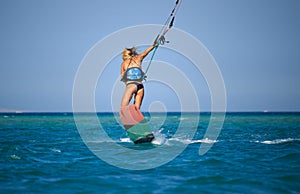 Kite surfing girl in sexy swimsuit with kite in sky on board in blue sea riding waves with water splash. Recreational activity,