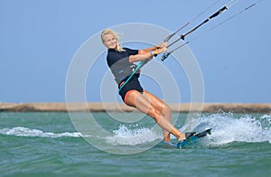 Kite surfing girl in sexy swimsuit with kite in sky on board in blue sea riding waves with water splash. Recreational activity,