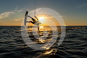 Kitesurfer doing handslide in sunset with sunstar and silhouette