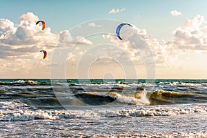 Kitesurfers ride kites through surfing waves of stormy sea at Blaga Beach resort at sunset