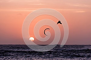 Kitesurfing jump, man kite surfer jumping at sunset golden hour silhouette on orange background