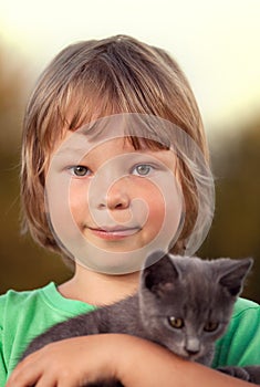 Kitten on arm of the boy outdoors, child huge his love pet