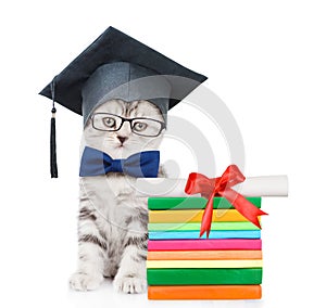 Kitten with black graduation hat sitting near books with diploma. isolated on white background