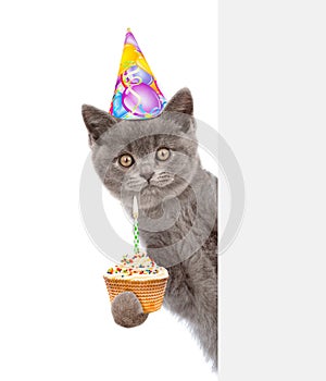 Kitten with cake in birthday hat looking out because of the poster. isolated on white background