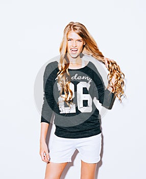 Kittenish Shouting Girl Pulling Her Hair. young woman in Sweatshirt and white shorts pulling ponytail and smiling. Indoor. Wa