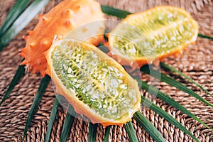 Kiwano or african horned melon with palm leaves on rattan background. Cutted hedged gourd, african horned cucumber, english tomato photo