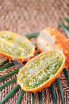 Kiwano or african horned melon with palm leaves on rattan background. Cutted hedged gourd, african horned cucumber, english tomato photo