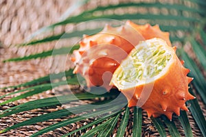 Kiwano or african horned melon with palm leaves on rattan background. Cutted hedged gourd, african horned cucumber, english tomato photo