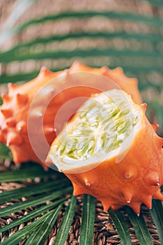 Kiwano or african horned melon with palm leaves on rattan background. Cutted hedged gourd, african horned cucumber, english tomato photo