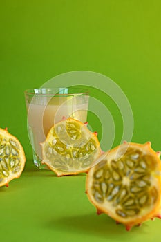 Kiwano slice, exotic vegetable cucumis metuliferus and a glass of fruit juice on a green background. Soft focus. Vegetarian food