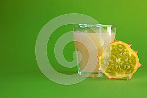 Kiwano slice, exotic vegetable cucumis metuliferus and a glass of fruit juice on a green background. Soft focus. Vegetarian food