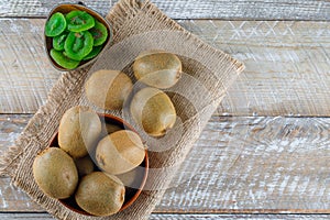 Kiwi in a bowl with dried slices flat lay on wooden and piece of sack background