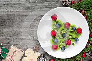 Kiwi christmas tree with fir tree branches and gift boxes over rustic wooden table. funny food idea for kids