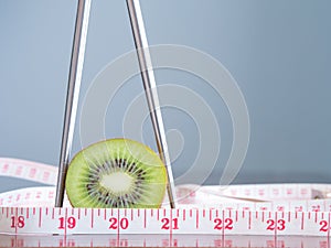 Kiwi fruit in chopsticks with measuring tape on a wooden table.