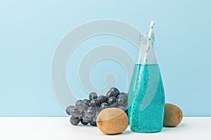 Kiwi fruit, grapes and a bottle of blue cocktail on a white table on a blue background