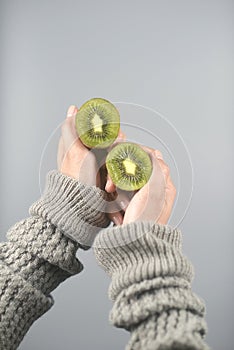 Kiwi fruit, half cut 2 pieces on women hands with sweater on light grey background. vertical image