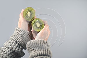 Kiwi fruit, half cut 2 pieces on women hands with sweater on light grey background.horizontal image