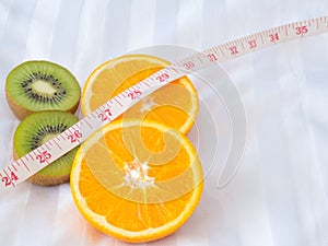 Kiwi fruit and Orange with measuring tape on bed.