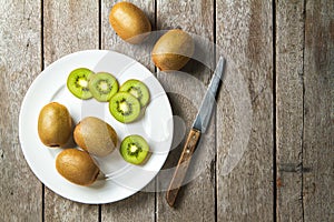 KIwi fruit on white dish and knife on wooden background.