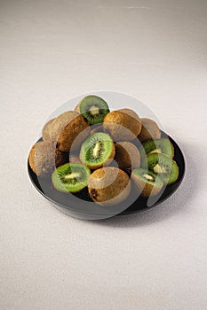 Kiwi fruits half sliced in black plate on vibrant plain white background