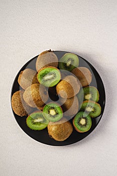 Kiwi fruits half sliced in black plate on vibrant plain white background