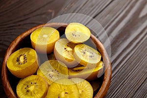 Kiwi Gold fruit slices in wooden bowl. Sliced kiwi with yellow flesh in salad dish on brown background. Juicy ripe healthy fruit