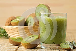 Kiwi smoothies in a glass next to fresh kiwi slices on a natural wooden table