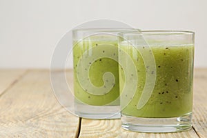 Kiwi smoothies in a glass next to fresh kiwi slices on a natural wooden table