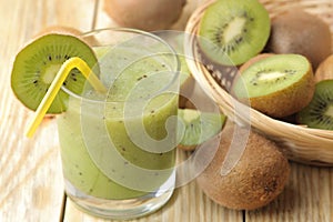 Kiwi smoothies in a glass next to fresh kiwi slices on a natural wooden table